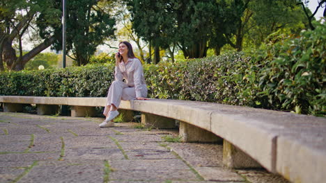 calling woman sitting park bench enjoy mobile conversation at sunny morning.