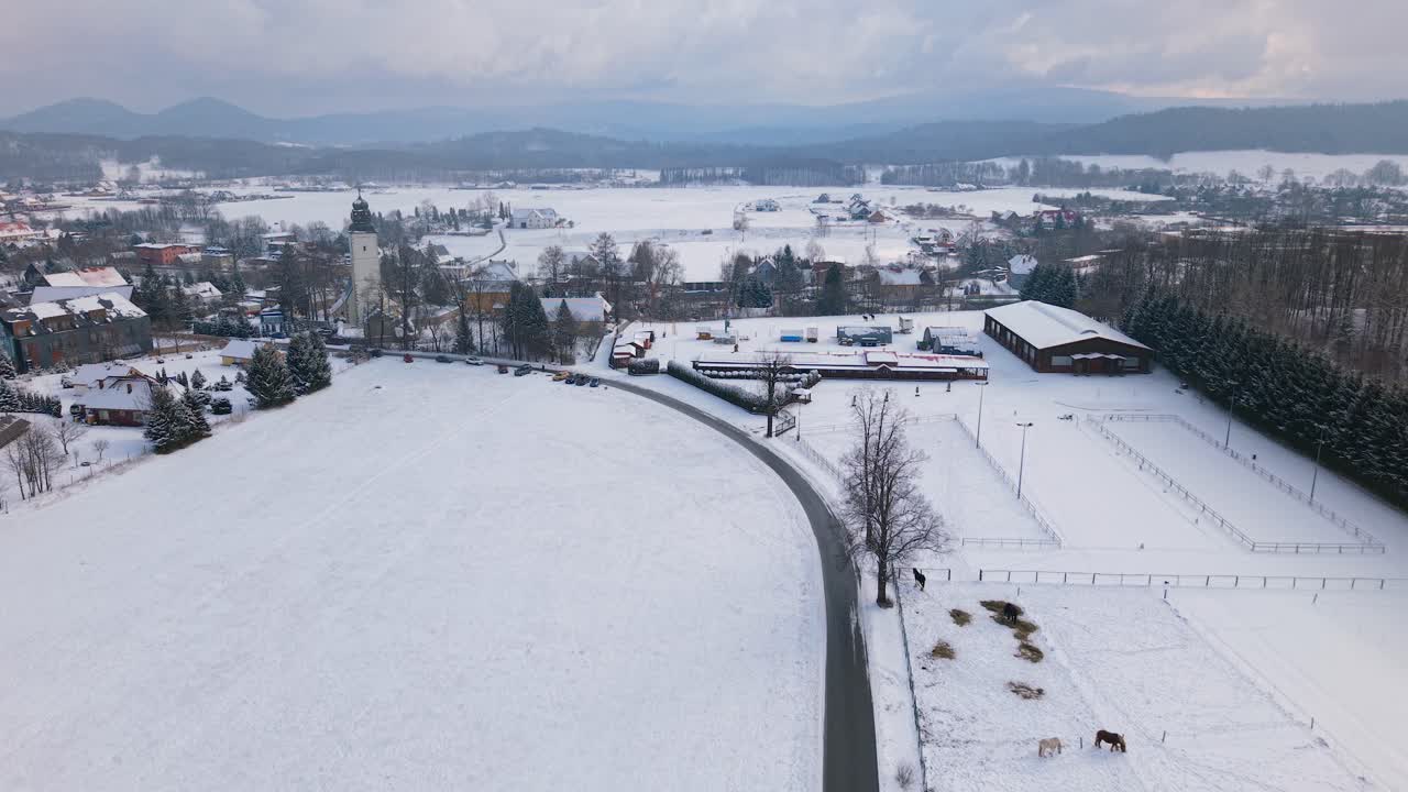 Aerial drone approach to a snow covered church in Lomnica, Poland, with the Karkonosze Mountains behind