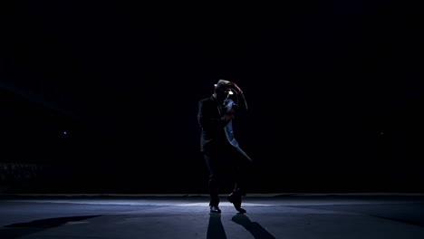 actor making funny dance on a stage. silhouette of a man in costume and hat dancing in dark background. amusing performance on scene.