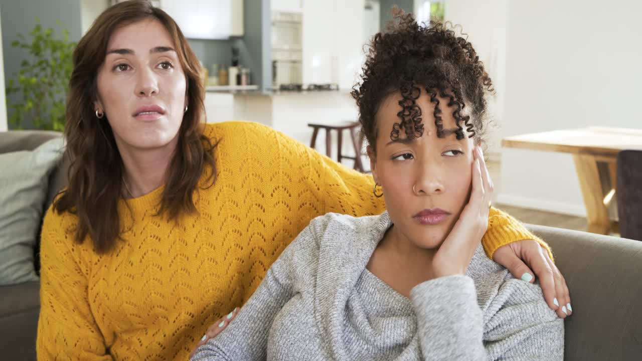 Amiche diverse che consolano un'amica affranta dopo un momento di pianto su un divano imbottito grigio.