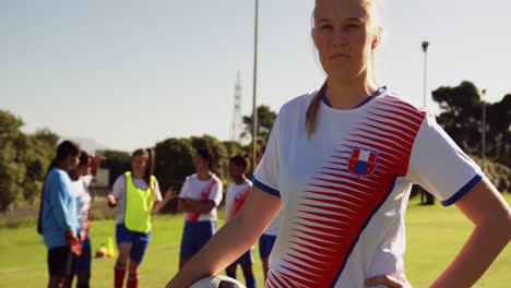 Female-soccer-player-holding-the-ball-while-teammates-talk-on-soccer-field.-4k