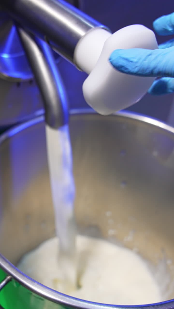 Worker at food factory opens the tap. Milk is poured into a metal bucket. Close up. Products for sweets production. Vertical video