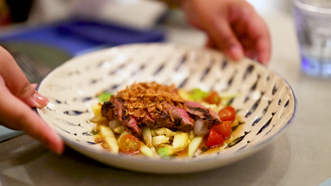 manos presentando un plato de ensalada de carne de res colorido