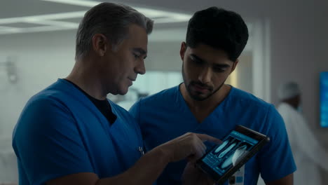 two medical professionals in scrubs examining medical scans on a tablet