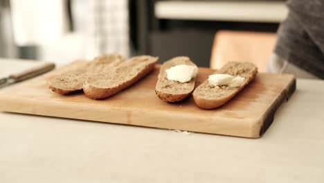 Man-spreading-creamy-cheese-on-a-brown-sliced-baguette-in-the-kitchen