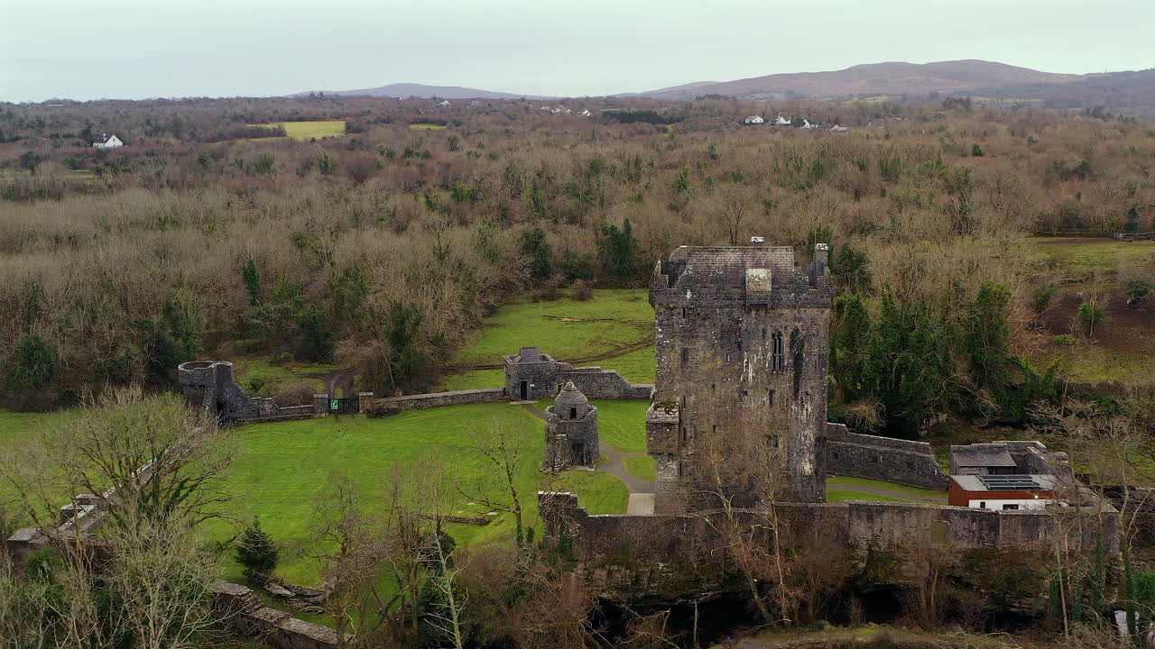Aerial establishing dolly over river to Aughnanure Castle in Ireland, surrounded by rolling hills and leaveless forests