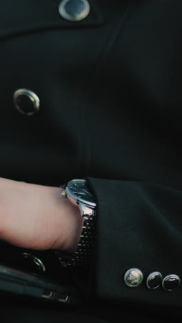 close up of individual hand in black suit operating laptop outdoors with attention to detail, featuring silver buttons, laptop ports, wristwatch, and soft bokeh background