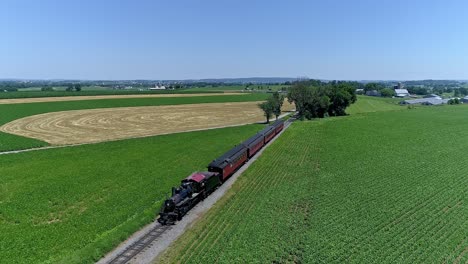 a vintage train glides smoothly along tracks surrounded by vibrant green fields and golden farmland under a clear blue sky