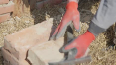 Worker-cleans-brick-from-mortar-and-place-it-on-pile,-deconstructing-old-house