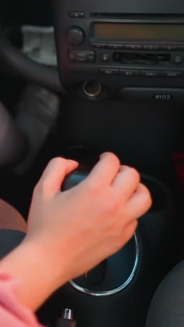 vista de la pierna de una mujer cambiando de marcha en su coche, moviéndolo hacia adelante y hacia atrás con una bolsa de compras visible y una taza de café cerca del cambio de marcha, las sombras de los coches que pasan se reflejan en ella mientras conduce