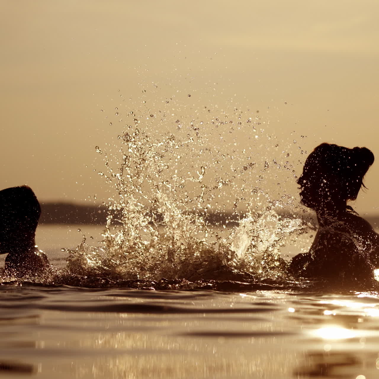 Mother and son in the river having great time together in the evening. Woman splashing water on a boy in the lake at dusk in summer time.