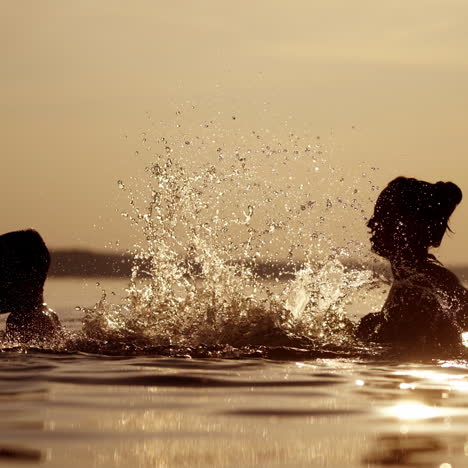 mother and son in the river having great time together in the evening. woman splashing water on a boy in the lake at dusk in summer time.