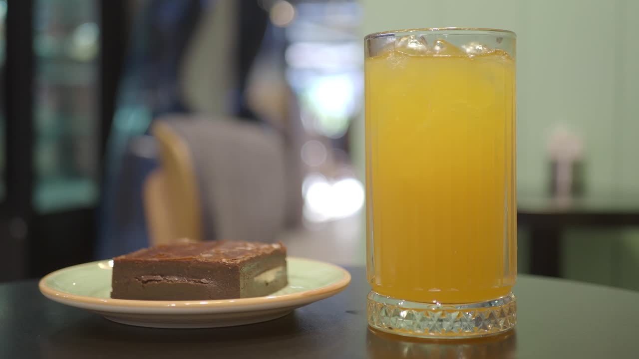 un vaso de jugo de naranja y un brownie en una mesa de café