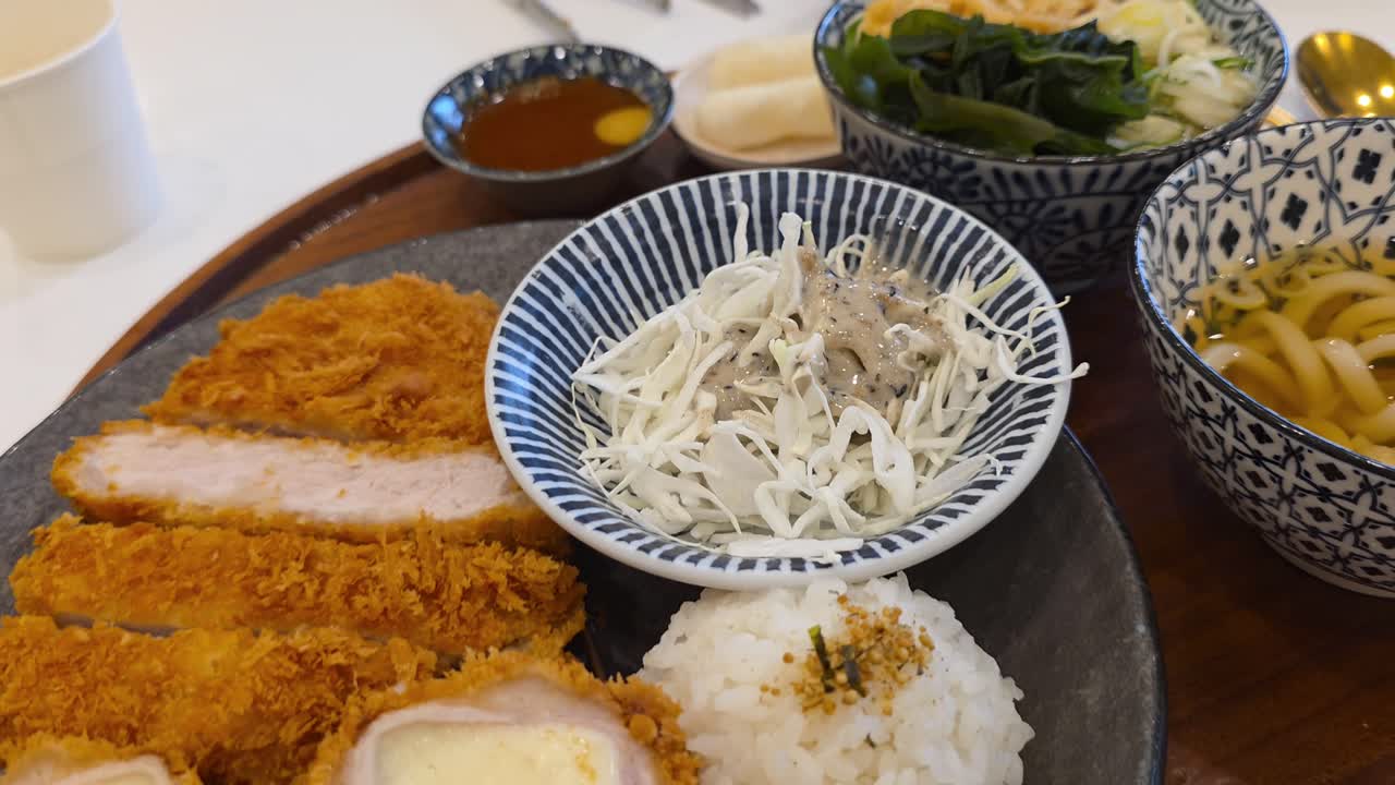 A delicious Japanese tonkatsu set meal (teishoku) served on a tray, featuring crispy original and cheese-filled pork cutlets with rice, shredded cabbage salad, and a bowl of udon noodle soup
