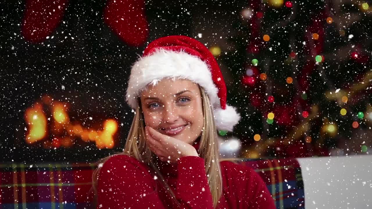 composición de video con nieve cayendo sobre chica feliz en traje de santa sentada en el sofá en la habitación con abeto