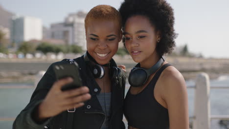 portrait of two beautiful african american woman uing phone on beachfront posing taking selfie