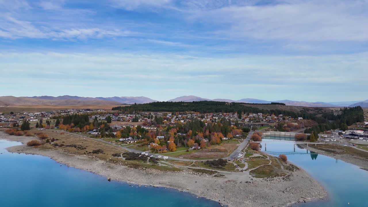 Drone footage captures Lake Tekapo's tranquil waters, surrounding town, and distant mountains under clear skies in Canterbury, New Zealand