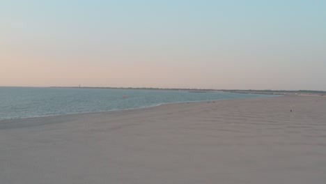 Cinematic-drone---aerial-shot-of-the-green-and-sandy-nature-beach-at-sunset-with-tourists-and-people-with-Buggykiting-at-Zeeland-at-the-north-sea,-Netherlands,-25p