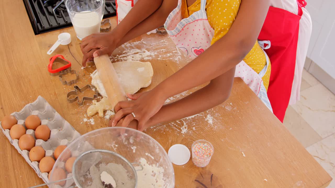 High angle view of black mother and daughter rolling dough in kitchen of comfortable home 4k