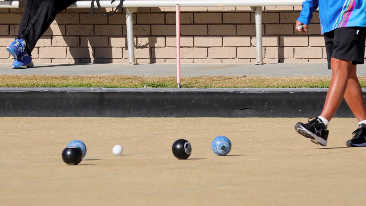 Players engage in a lawn bowls game on a sunny day, showcasing precise movements and strategic gameplay