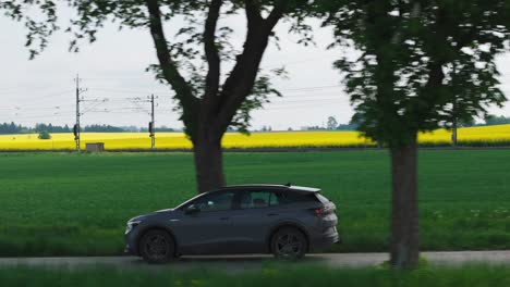 Ein-EV-Geländewagen-Fährt-Durch-Eine-Schattige-Straße,-Während-Der-Zug-Hinter-Ihm-Vorbeifährt,-Seitliche-Verfolgung