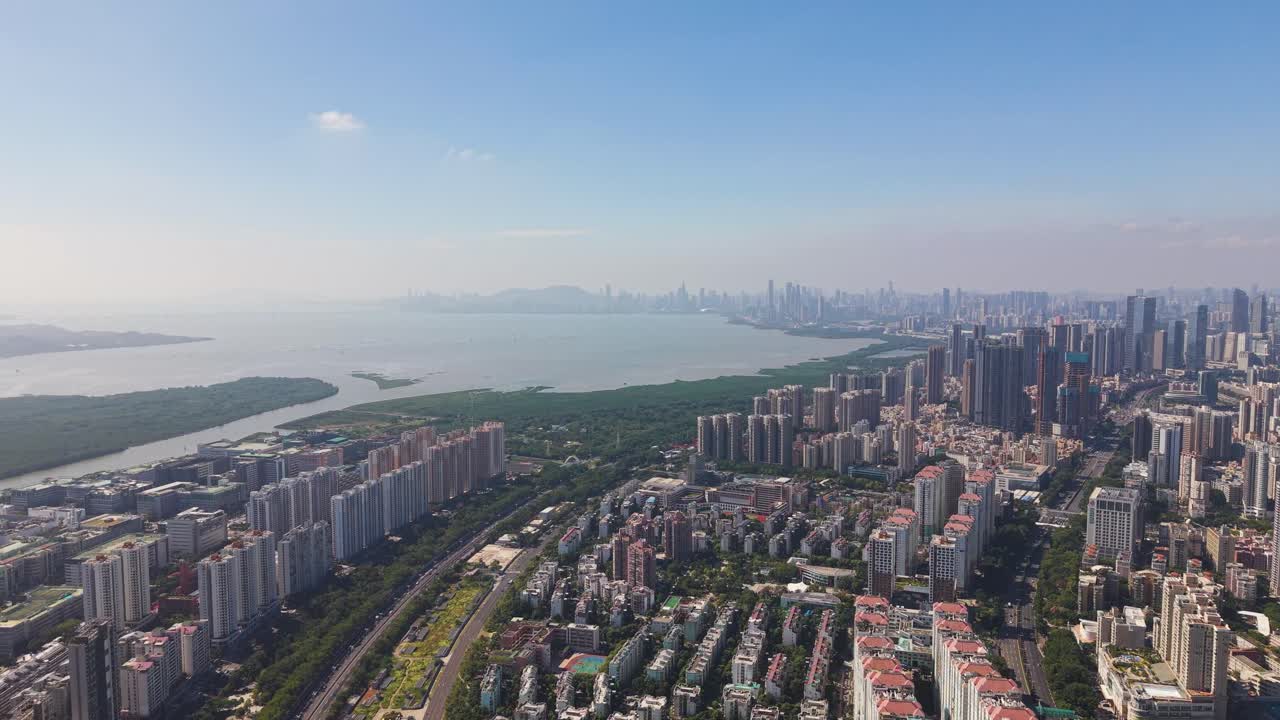 Wide aerial view of Shenzhen Bay with dense skyline, calm water and sprawling urban districts under clear daylight, capturing the scale, growth and modern character of this coastal Chinese megacity