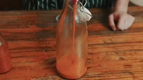 pouring creamy red pepper sauce in a glass bottle for storage