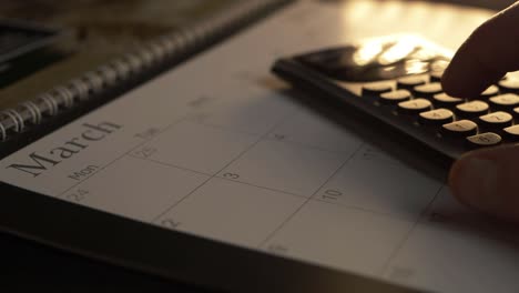 Hand using calculator on March calendar close up
