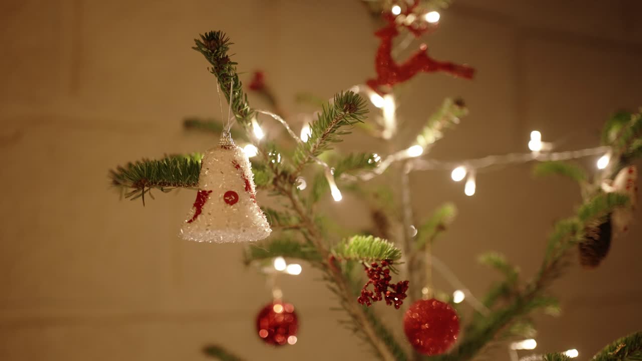 primer plano del árbol de navidad con campana y adornos rojos brillando bajo las luces.