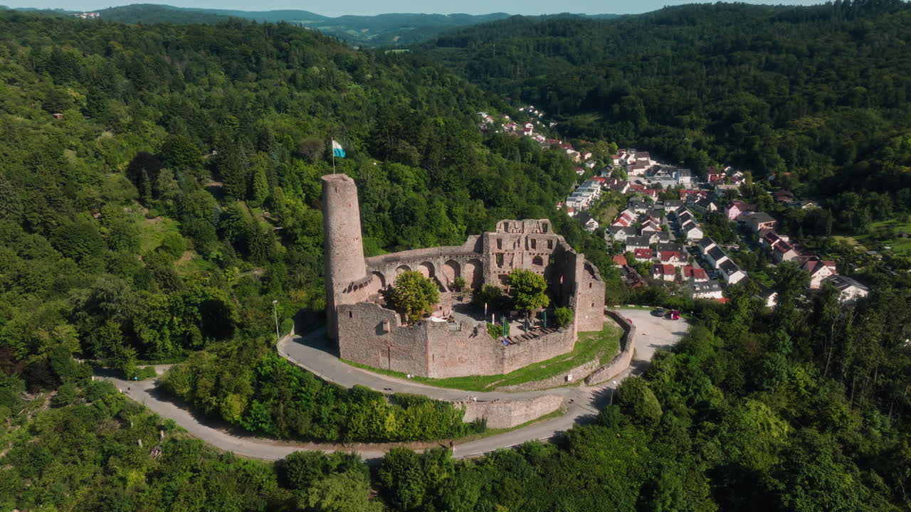 Aerial drone orbiting around the ruins of Dilsberg Castle near Heidelberg, Germany, surrounded by forested hills and a winding road leading to the site