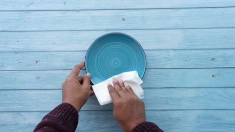 person cleaning a blue plate with a white napkin