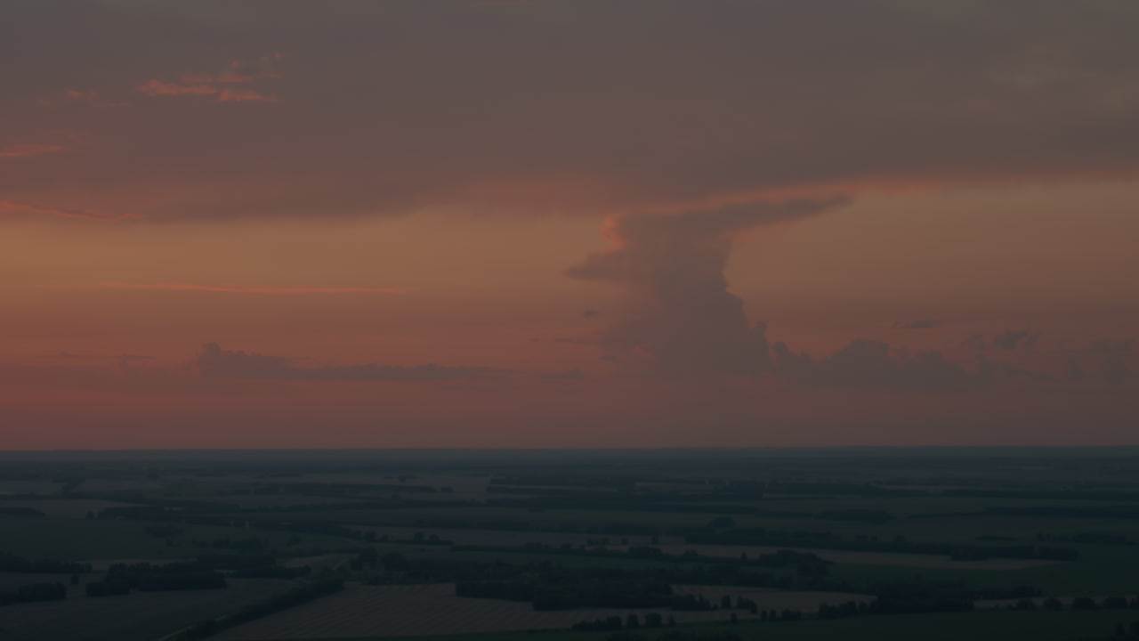 Towering dusk cloud formation illuminated by deep orange sunset glow over expansive horizon, sky layered in dramatic shadows and warm hues