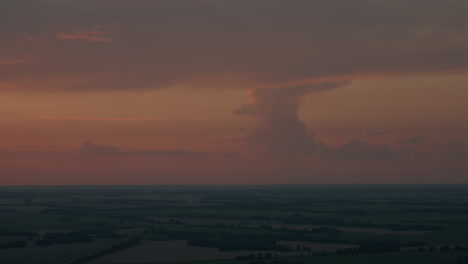 towering dusk cloud formation illuminated by deep orange sunset glow over expansive horizon, sky layered in dramatic shadows and warm hues