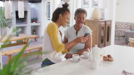 African-american-mother-and-daughter-smiling-while-using-smartphone-together-at-home