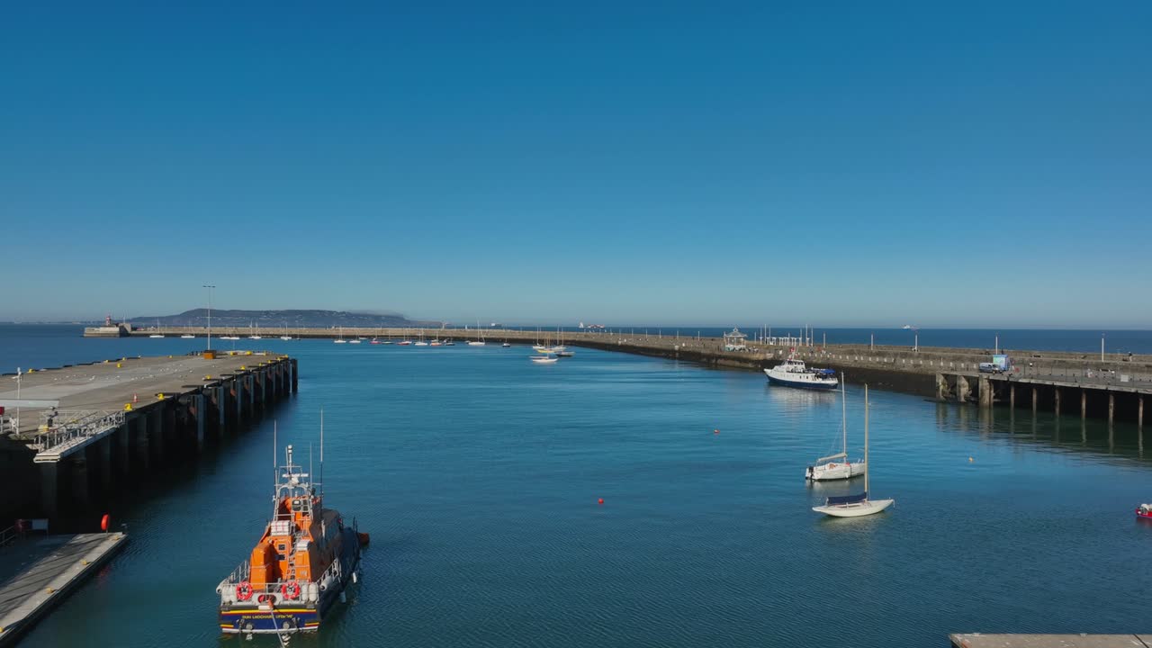 Dublin Bay Cruises Boat, Dún Laoghaire, County Dublin, Ireland, September 2024. Drone slow dolly passes the Royal National Lifeboat in the Harbour as commuter tour boat departs from the East Pier.