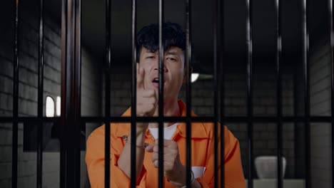 close up of asian male prisoner in handcuffs standing in prison, pointing his finger towards you, speaking against and blaming you