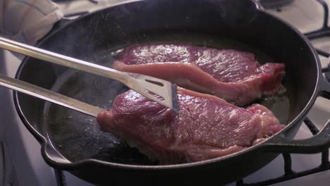 steaks being cooked and flipped in a cast iron skillet with oil - slow motion