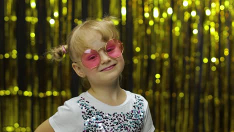 Child-smiling,-looking-at-camera.-Girl-in-pink-sunglasses-posing-on-background-with-foil-curtain
