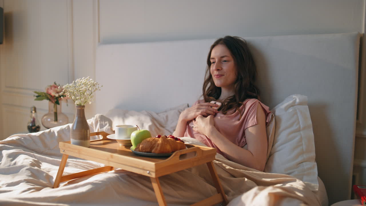 침대에서 집에서 휴식을 취하는 즐거운 소녀. 드폰을 들고 있는 아름다운 만적인 여자