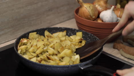 caucasian right hand stirs potatoes in pan with wood spatula, close up