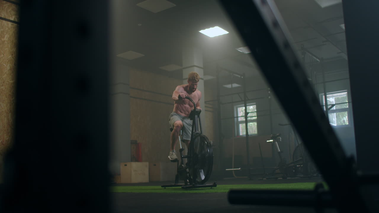 Giovane uomo che usa la cyclette in palestra. Un atleta si allena con una air bike per un allenamento cardio. Sforzo con l'attrezzatura.
