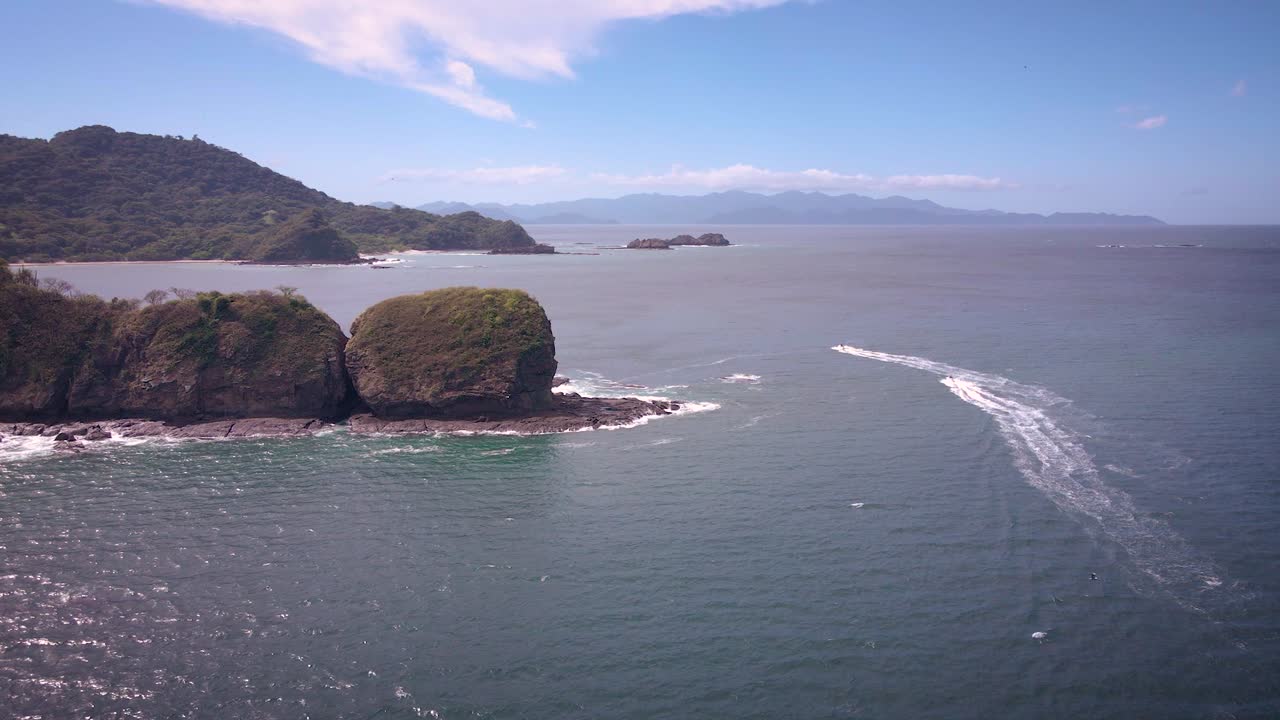 Ripresa con drone di alcune isole al largo della costa del Costa Rica con una fregata che vola vicino al drone e moto d'acqua che sfrecciano in lontananza