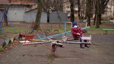 a boy in a medical mask ride on a swing 02