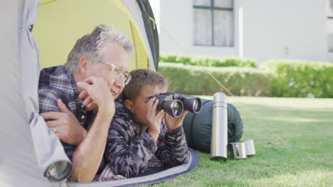 Happy-caucasian-grandfather-and-grandson-sitting-in-tent-and-looking-through-binoculars,-slow-motion