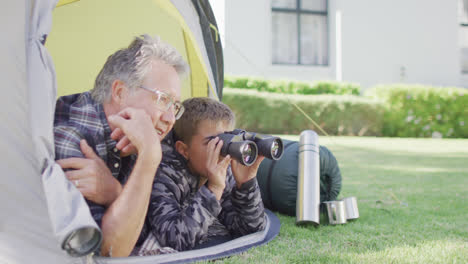 happy caucasian grandfather and grandson sitting in tent and looking through binoculars, slow motion