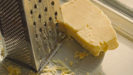 block of cheese on plate with grater and with pieces of cheddar on plate as camera slowly rotates in natural light. dairy based organic food