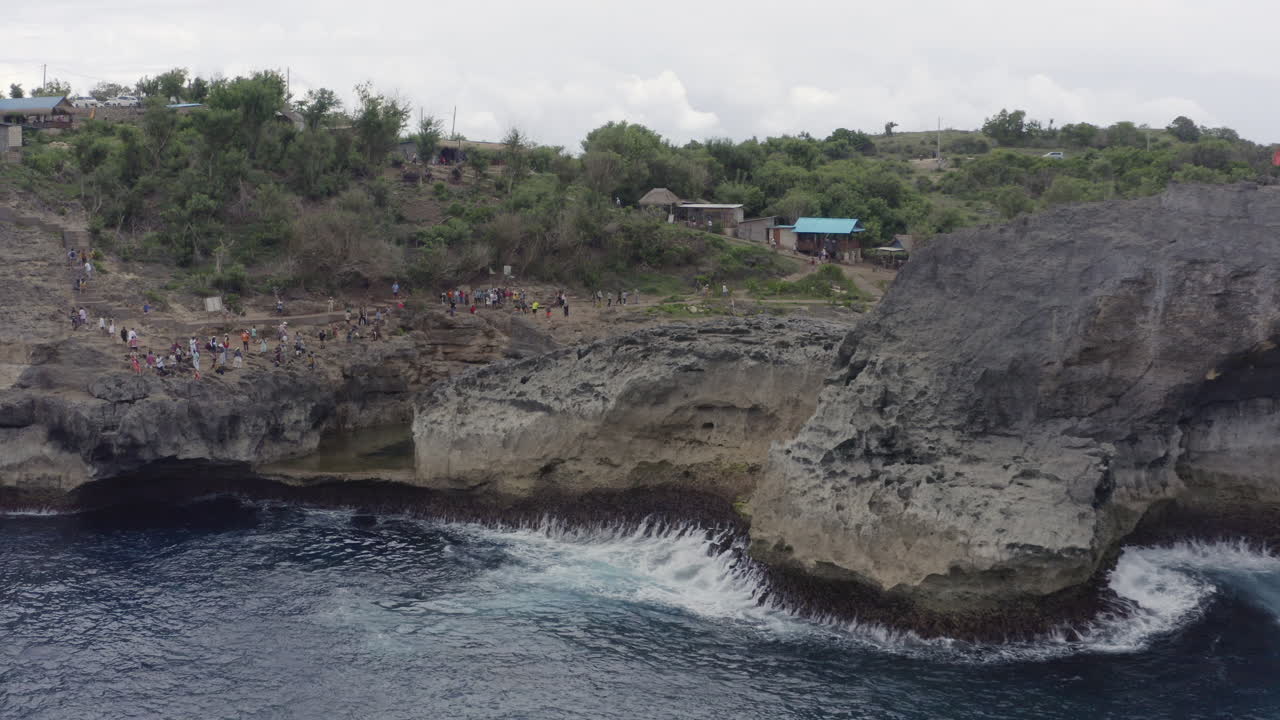 High steep coast of Broken Beach, with lagoon trench, and numerous tourists taking photographs on its sides.Nusa Penida, Bali, Indonesia. Aerial shot