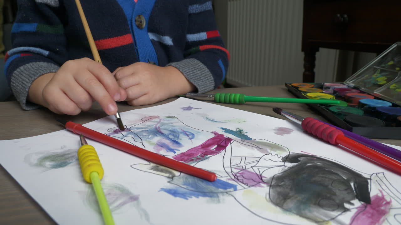 어린 소년이 수채화 페인트 브러시를 사용하여 책상에 앉아 있는 중간 클로즈업