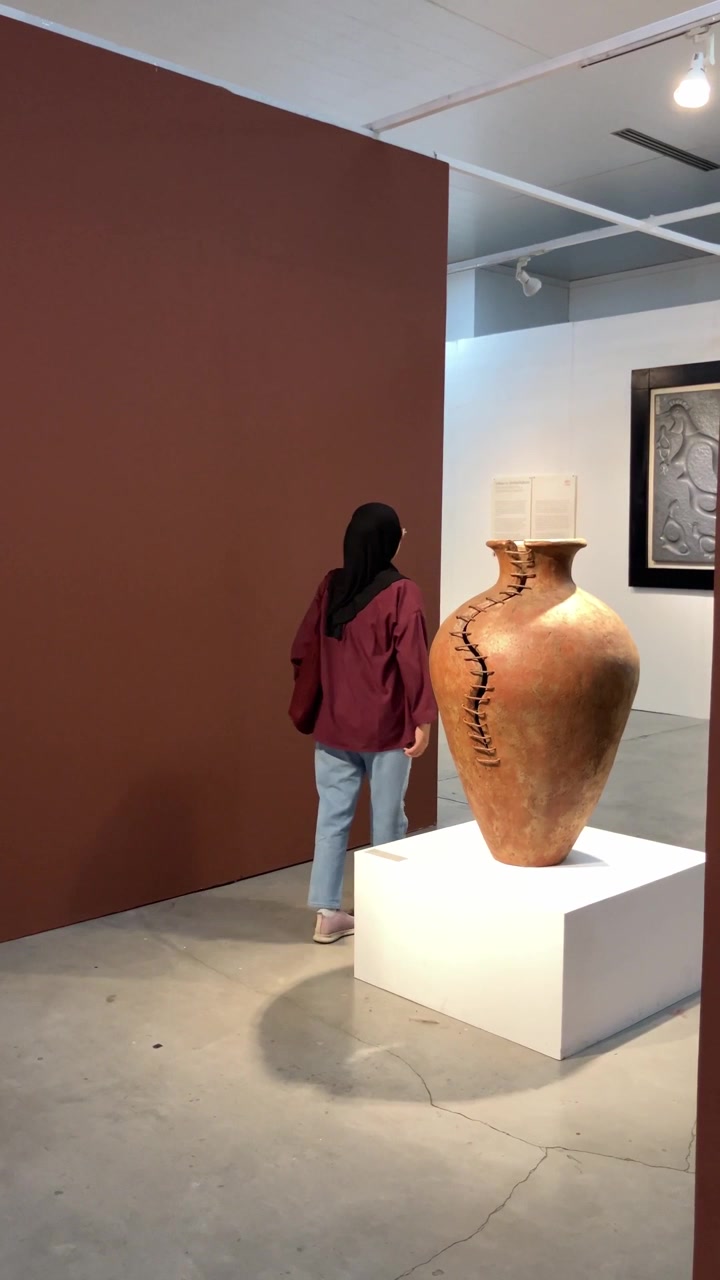 Clip al rallentatore di una giovane donna musulmana con hijab che cammina in una galleria d'arte, osservando una mostra di grandi vasi in ceramica di terracotta. Concetto di arte culturale e stile di vita museale