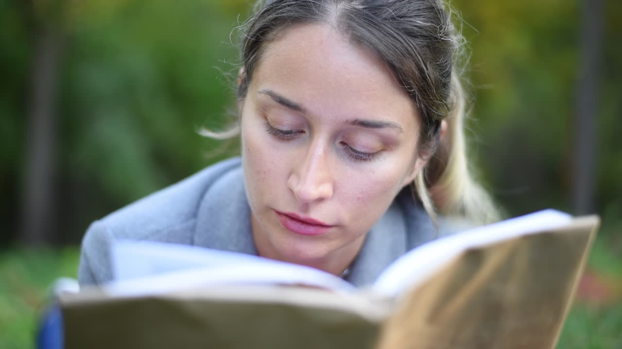 Blonde woman reading a book, lying on the grass in a park